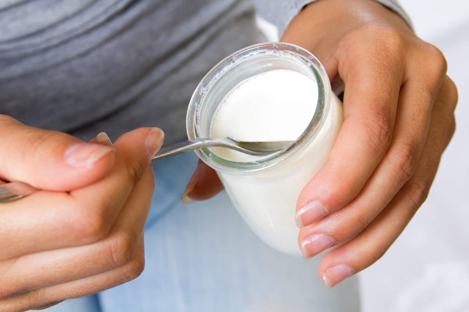 close-up-of-womans-hands-holding-jar-of-white-yogurt-and-spoon