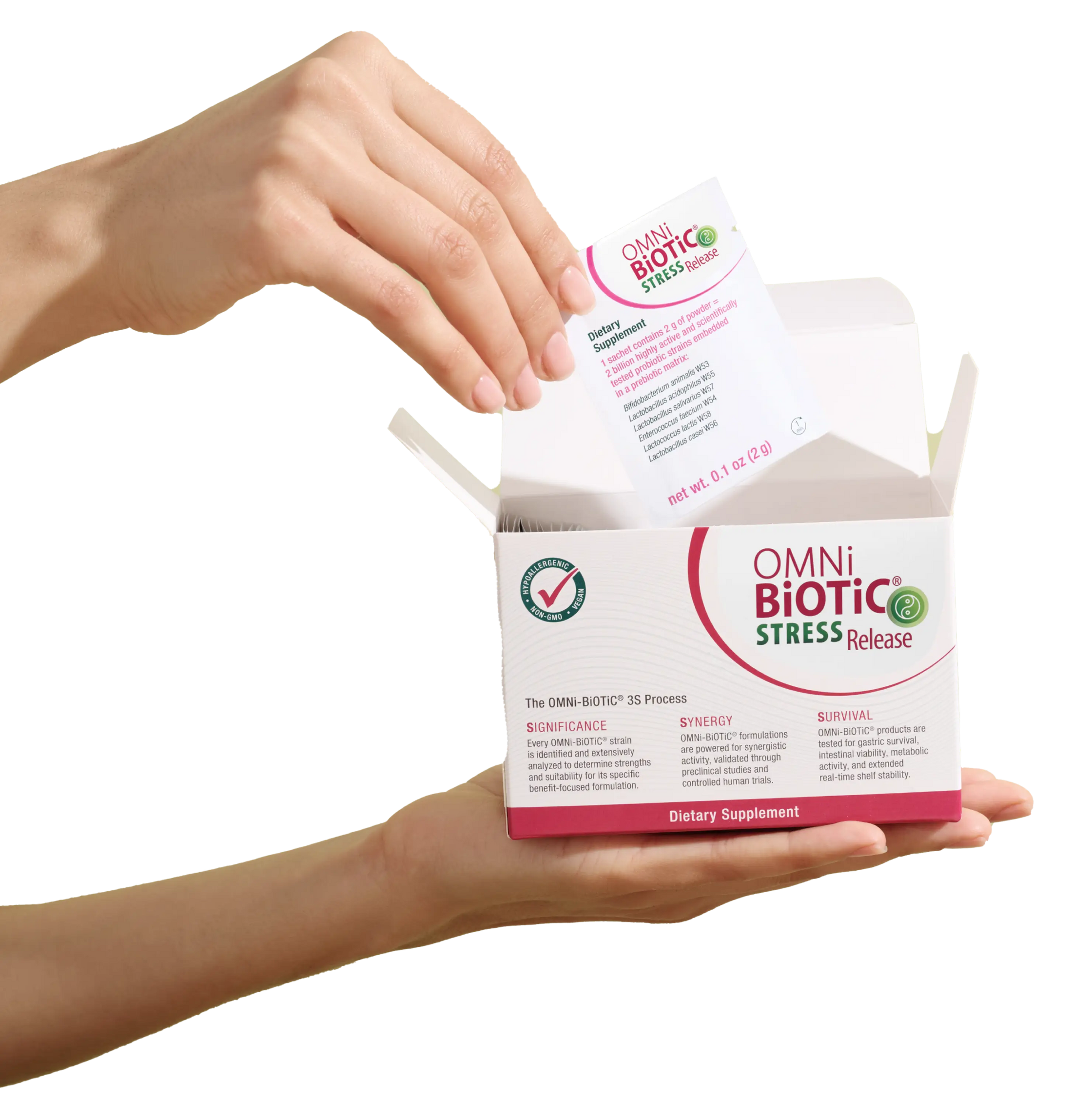 A hand holding an open box of Omni-Biotic Stress Release probiotic supplements with a sachet being pulled out.