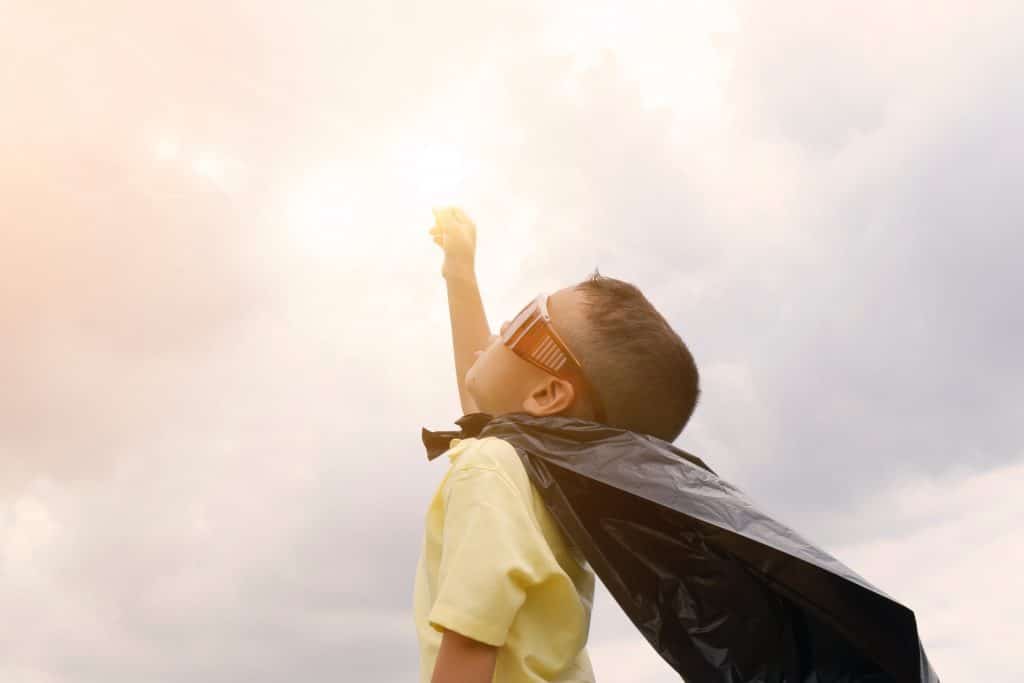 young-boy-wearing-superhero-costume-raising-his-fist-to-the-clouds