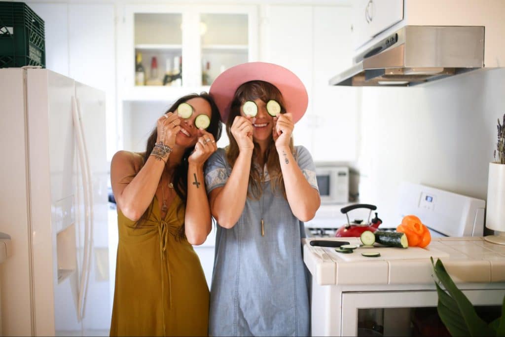 Two women smiling with cucumbers over their eyes.