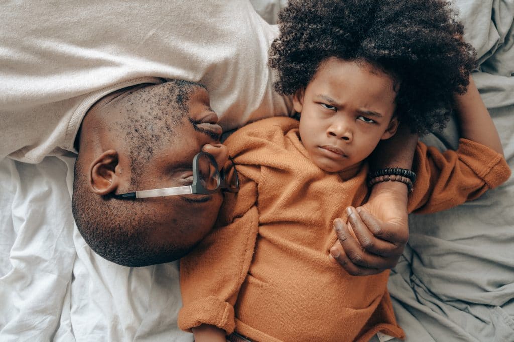 napping-father-and-grumpy-child-laying-on-bed-with-white-sheets