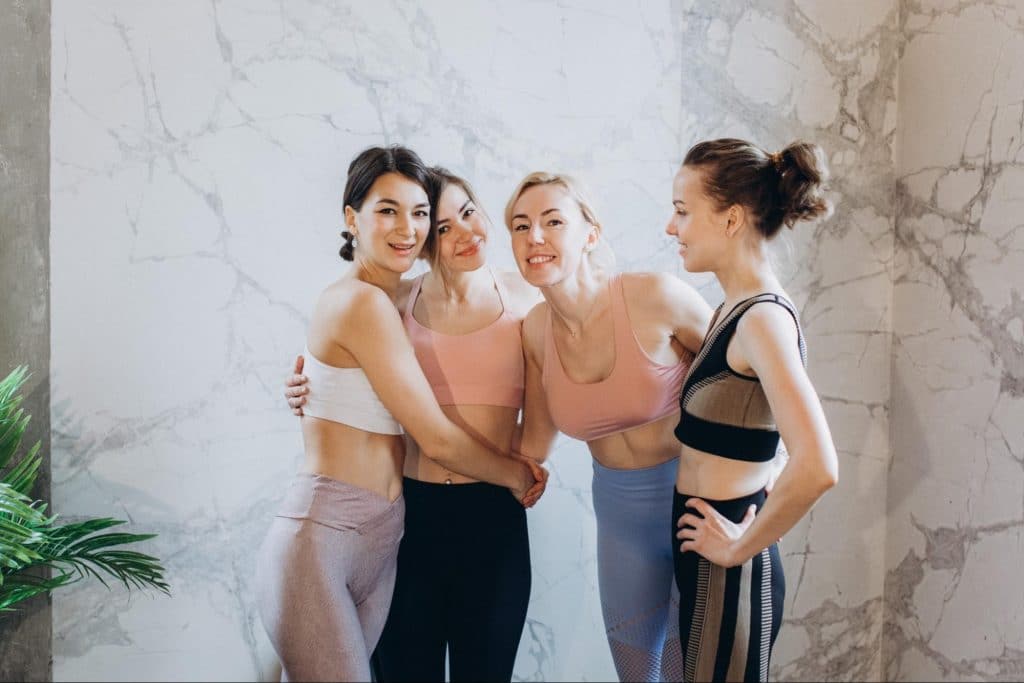 four women in exercise gear group hug