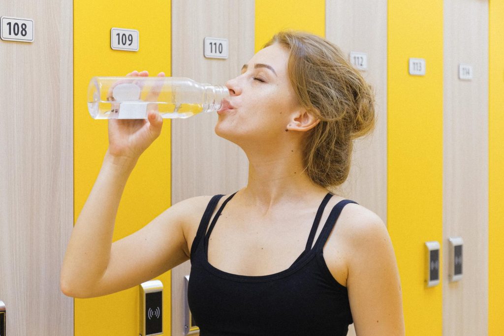 A healthy young woman drinking water in a gym. Taking prebiotic supplements at the same time every day with water helps make them the most effective.