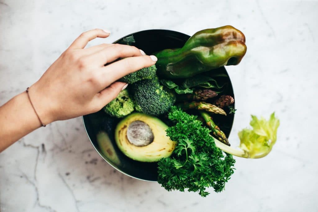 Healthy green vegetables including artichokes, avocados, broccoli, kale, and bell peppers in a bowl. Some of these vegetables are excellent sources of prebiotic fiber which are helpful for the good bacteria in the gut.