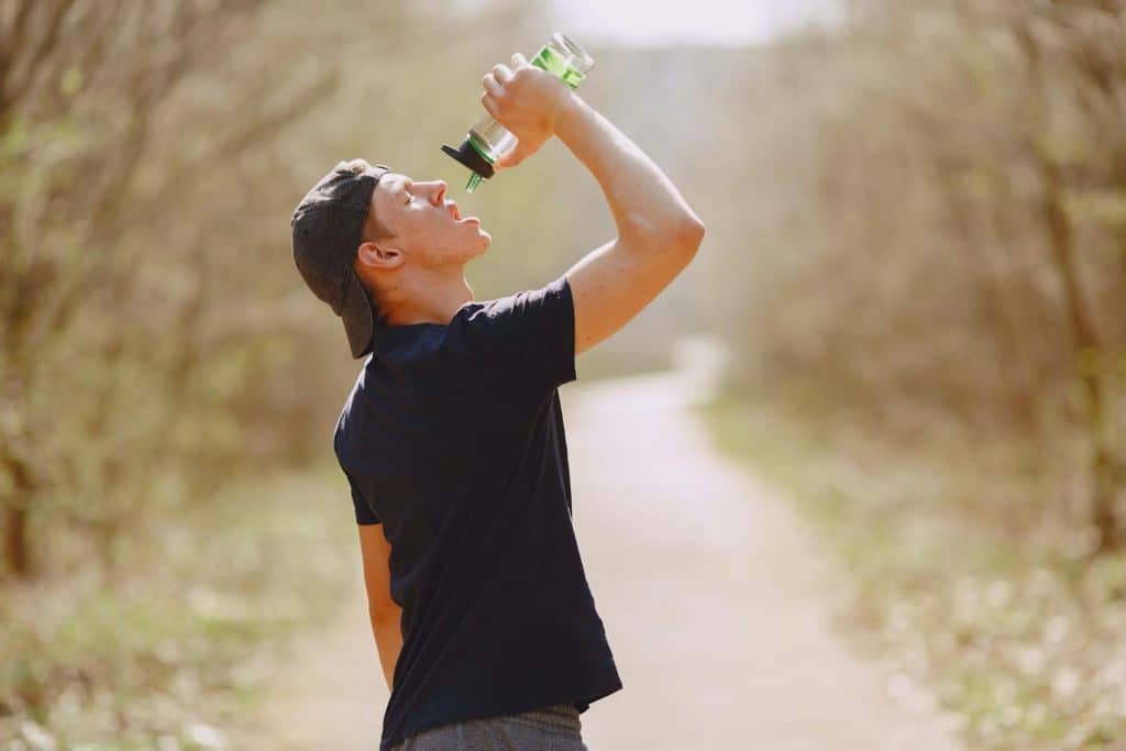 man drinking water from a bottle to rehydrate while on a walk