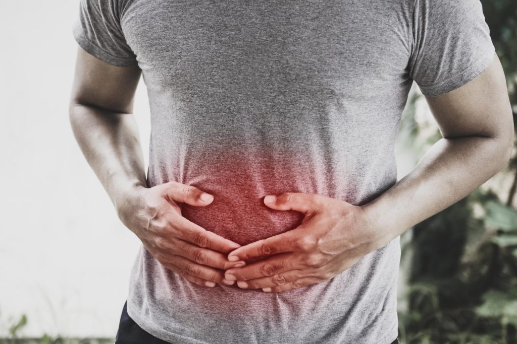 A man holds his painful stomach while suffering with Irritable Bowel Syndrome. Prebiotics and probiotics may help with IBS.