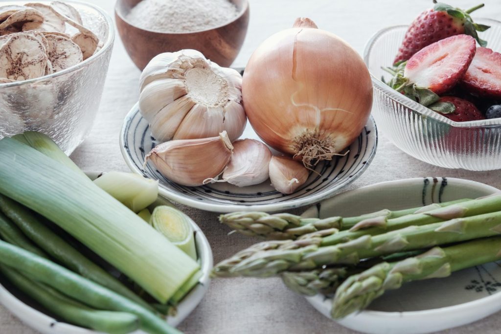 An assortment of prebiotic foods including garlic, strawberries, onions, leeks, and asparagus.