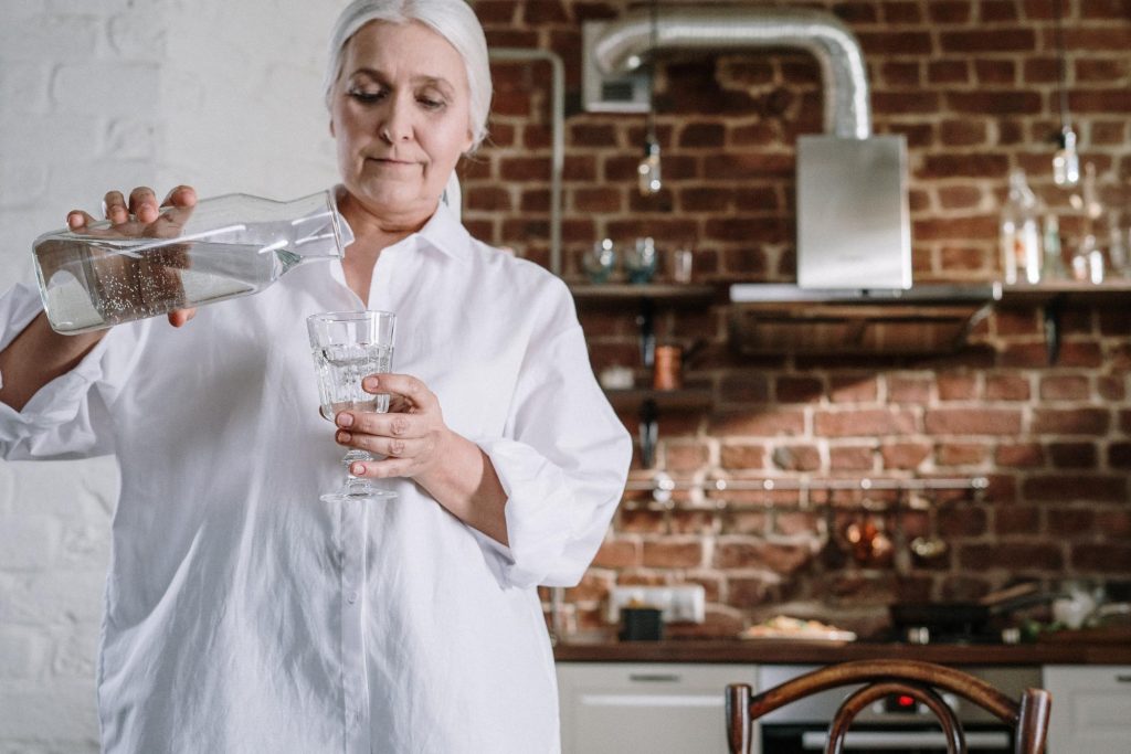 senior woman in her kitchen pouring herself glass of water