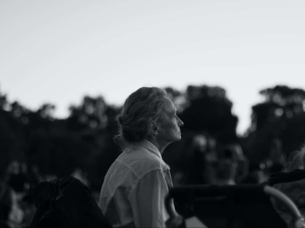 black and white photo of a senior woman sitting on a park bench facing away form the camera