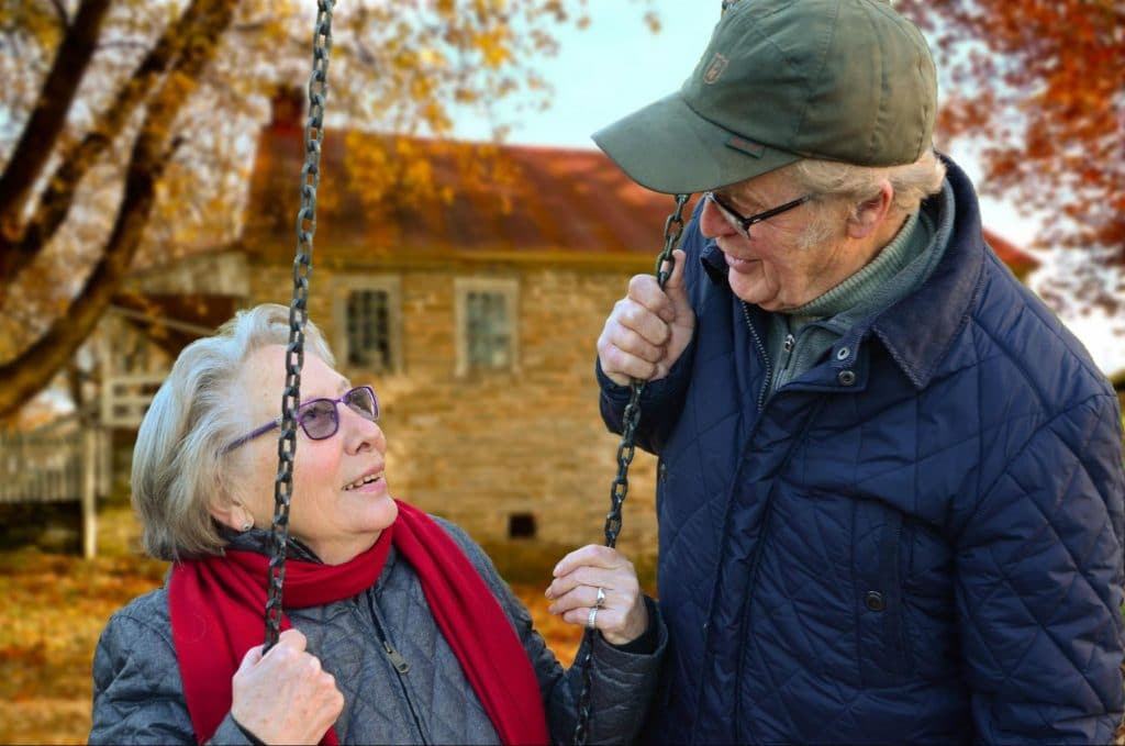 senior couple smiling and laughing at one another on a swingset in a park