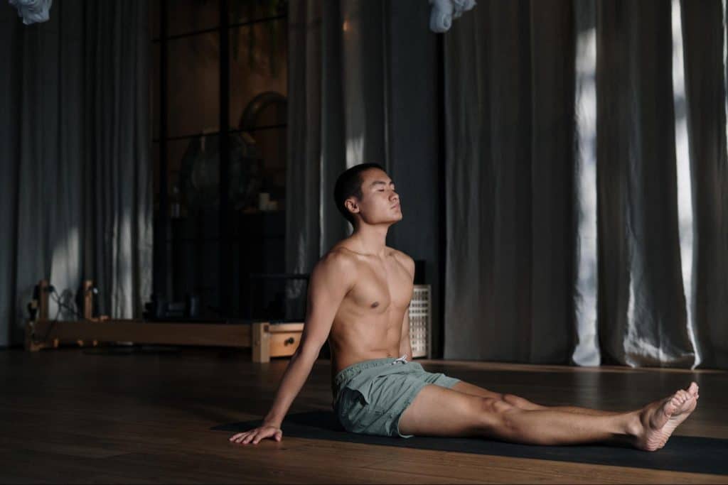 Fit man sitting on yoga mat doing yoga pose.