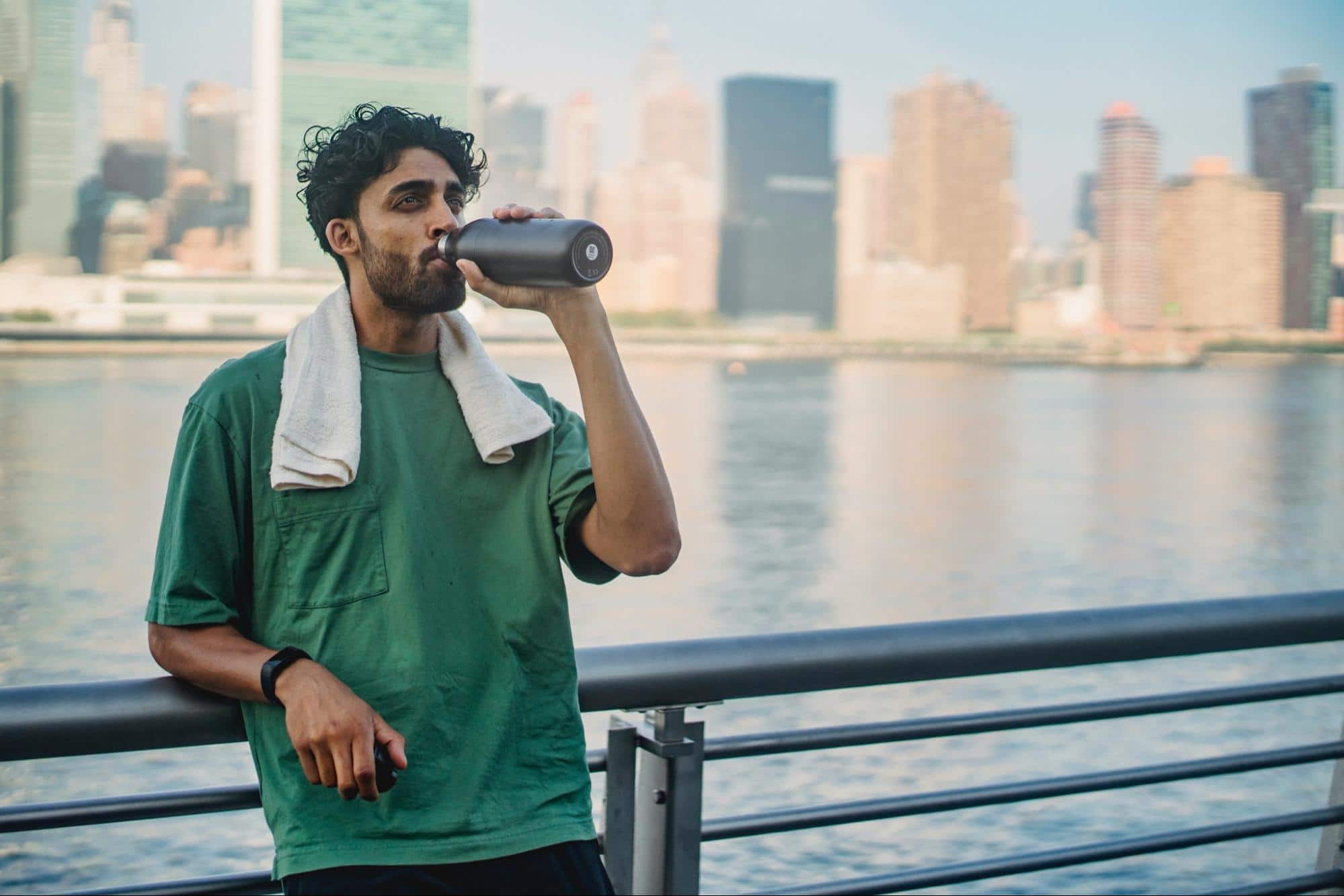 A male runner taking a break to drink water leaned against bridge railing.