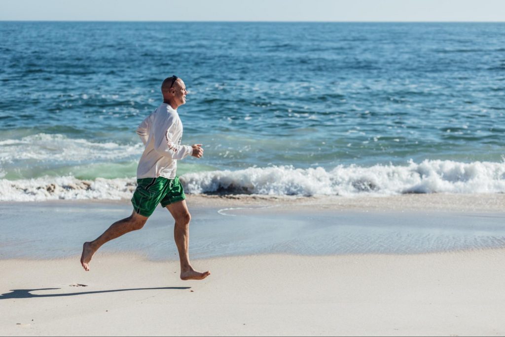 A man running across beach with waves in the background.