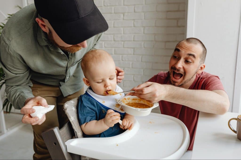 Smiling parents feed baby in high chair