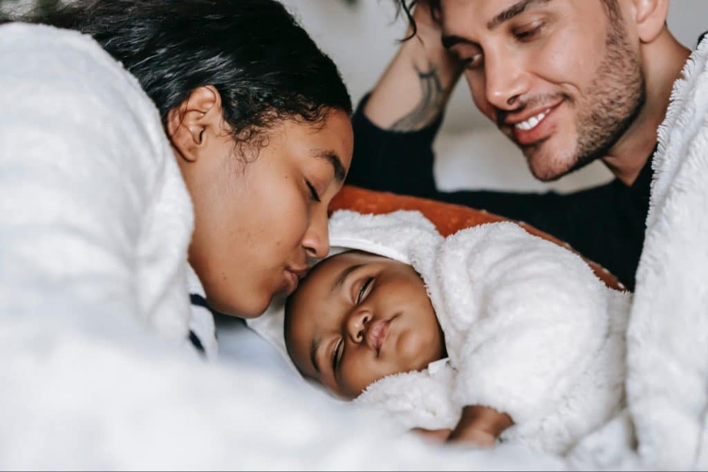 Smiling parents in bed with new baby