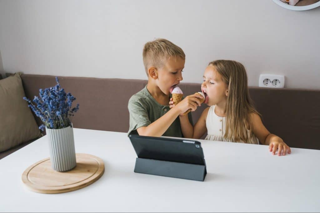 Two kids eating ice cream and using tablet computer.