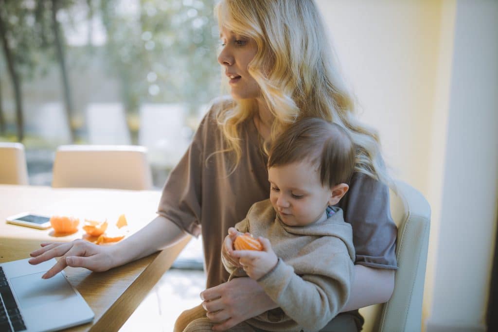 woman-holding-her-baby-while-working-on-a-laptop