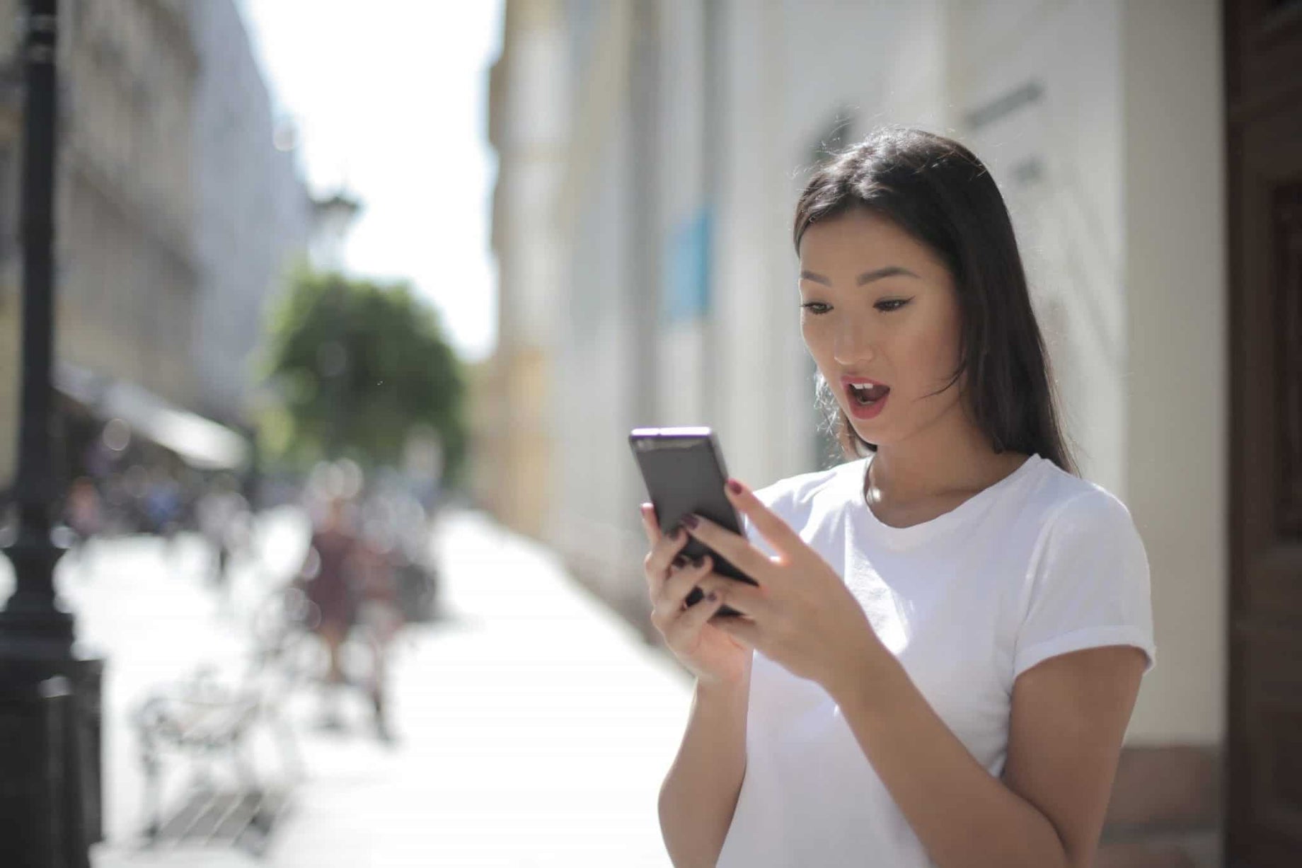 woman-in-white-crew-neck-t-shirt-holding-black-smartphone-with-shocked-expression-on-face