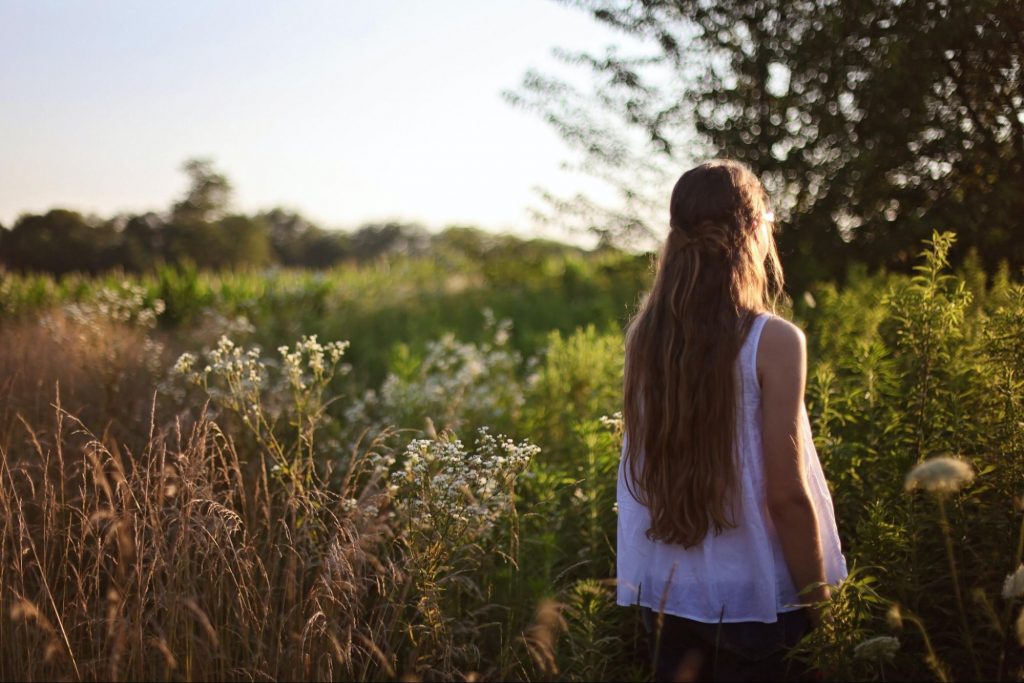 A woman in a white shirt walks through a meadow.