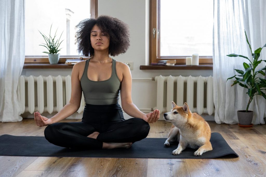 Woman in yoga pose with a dog sitting next to her. Regular exercise and a healthy diet full of prebiotic and probiotic foods can help with weight loss.